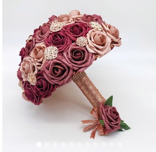 Dusty rose, mauve, and burgundy bridal bouquet made with real touch roses. Handle is made using rose gold ribbon finished with rose gold bling wrap. Rose gold brooches are scattered throughout bouquet