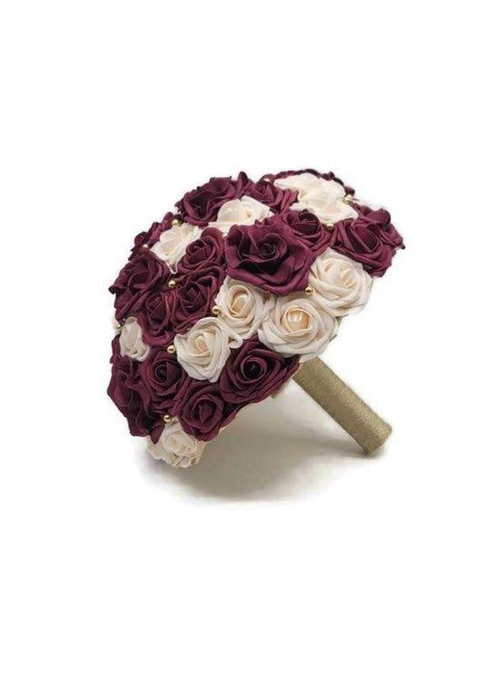 Burgundy and cream real toch roses with a mix of avalanche roses and gold balls. Handle is made up of gold ribbon. 