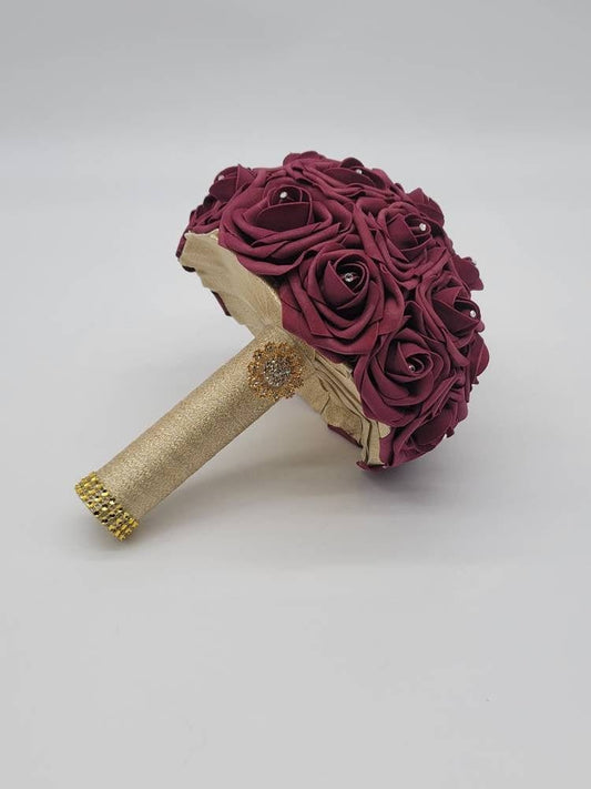 Burgundy and gold wedding bouquet made with RealTouchRose. Rhinestonesare in the center of every rose. Handleis made using Gold ribbon and finished with Goldbrooch and bling wrap.