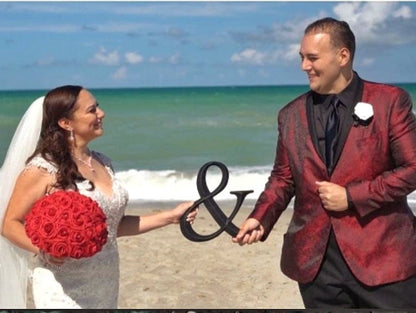 Bride and Groom holding Red real touch rose bouquet with black satin ribbon handle. Silver bling wrap on handle. Rhinestones on every rose.