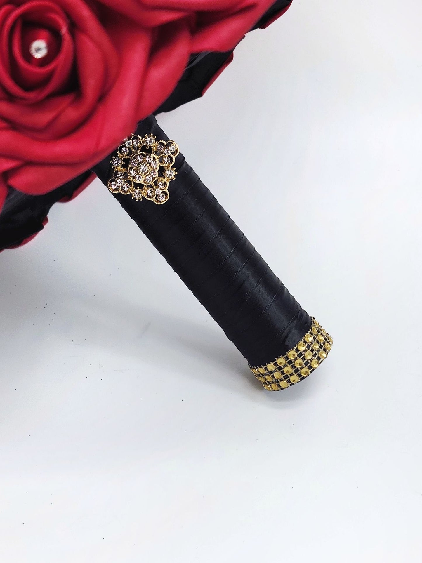 Close up of handle. Red real touch rose bouquet with black satin ribbon handle. Gold bling wrap and brooch on handle. 