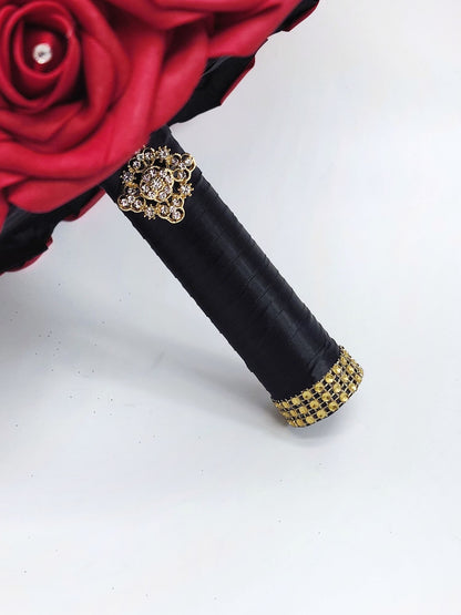 Close up of handle. Red real touch rose bouquet with black satin ribbon handle. Gold bling wrap and brooch on handle. 