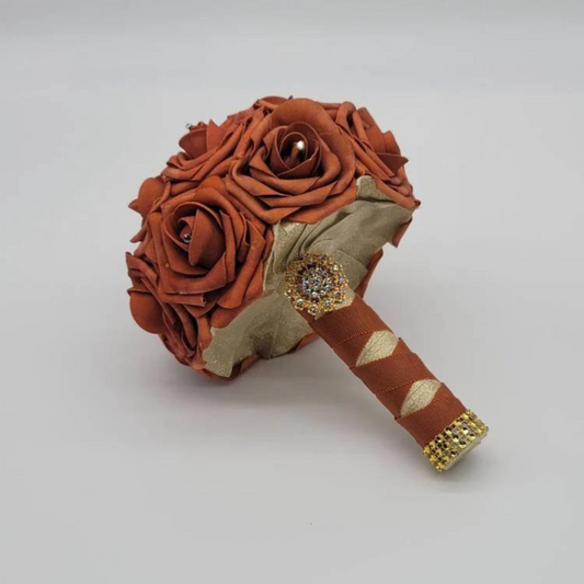 burnt orange bridal bouquet with gold and burnt orange ribbon handle in a french twist with gold brooch and gold bling wrap