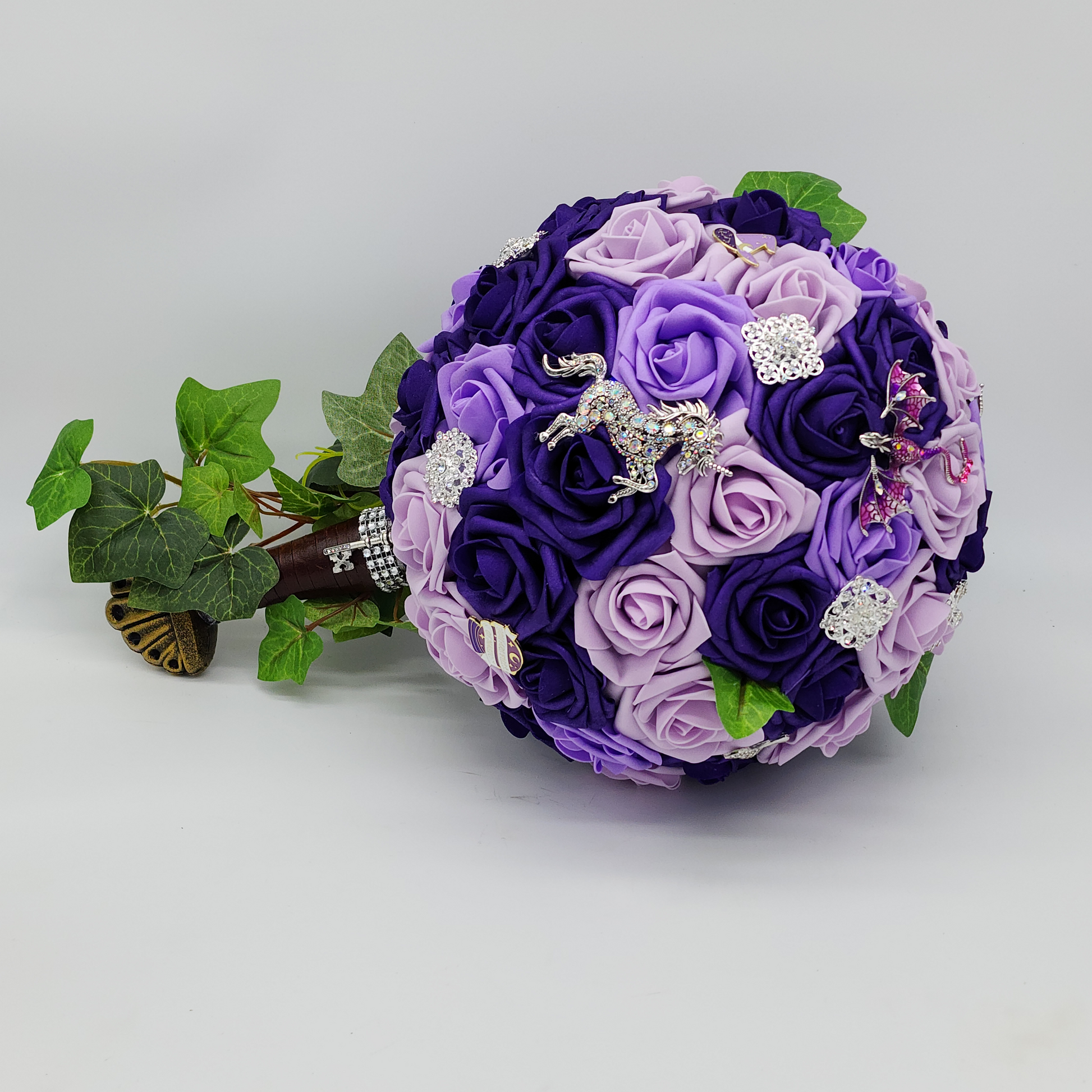 purple bridal bouquet with sword handle. fantasy brooches are scattered on bouquet. unicorns, dragons. ivy handle